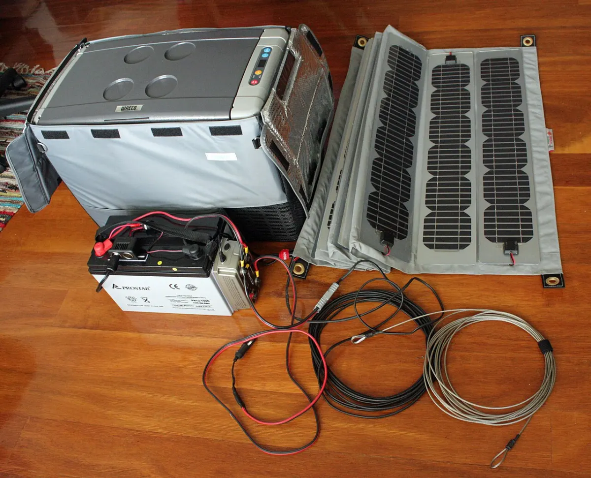 Portable camping solar panel, 12V battery and portable refrigerator laid out for a power-system setup